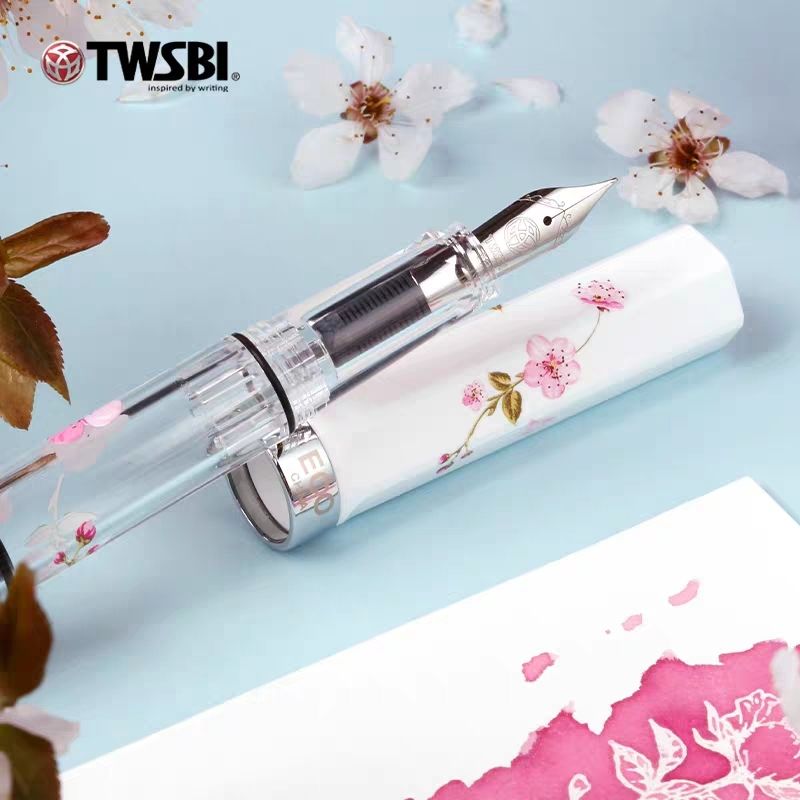 TWSBI ECO Sakura fountain pen lying beside its white cherry blossom cap on a blue background